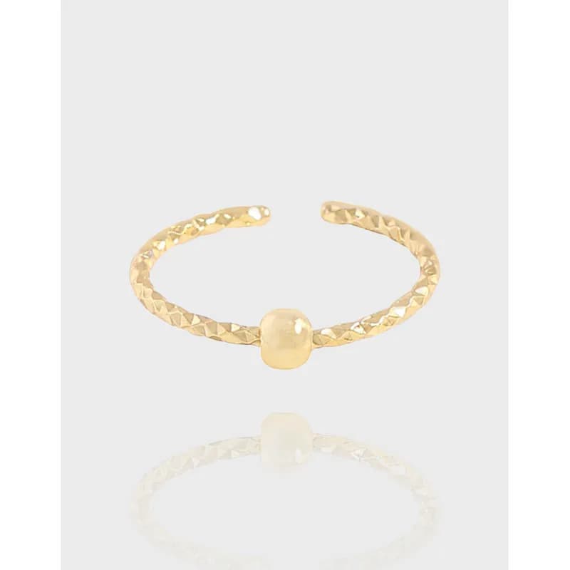 Gold-toned sterling silver ring with a textured band and a single central bead on a white background.