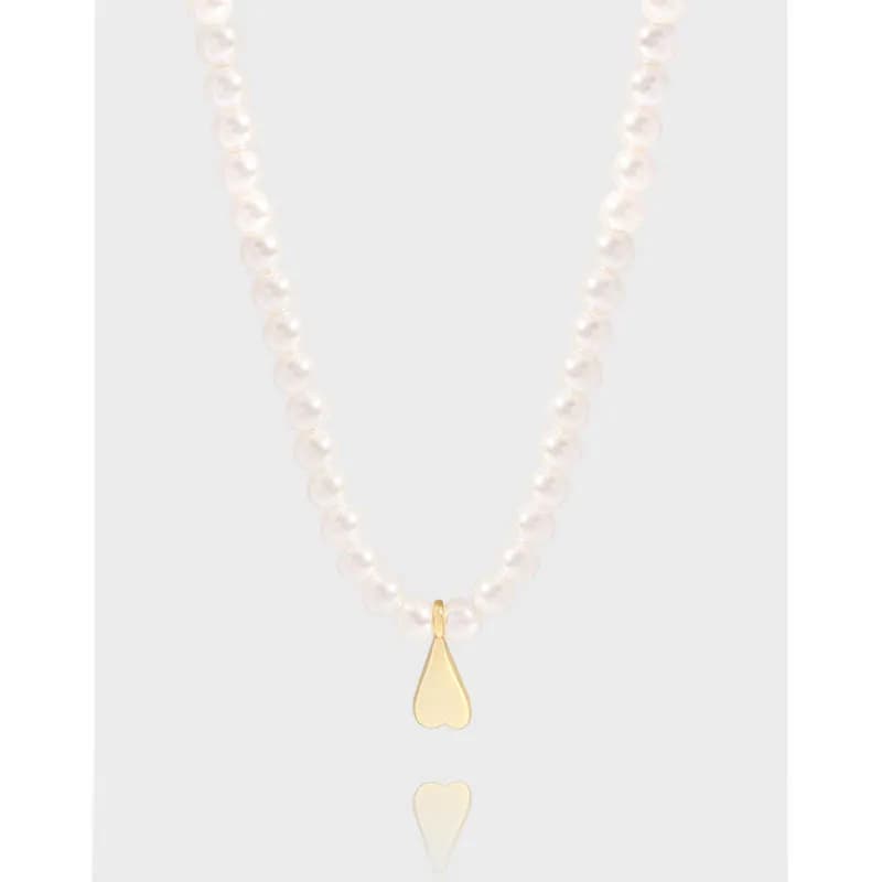 Pearl-like bead necklace with a small gold teardrop heart pendant on a neutral background.