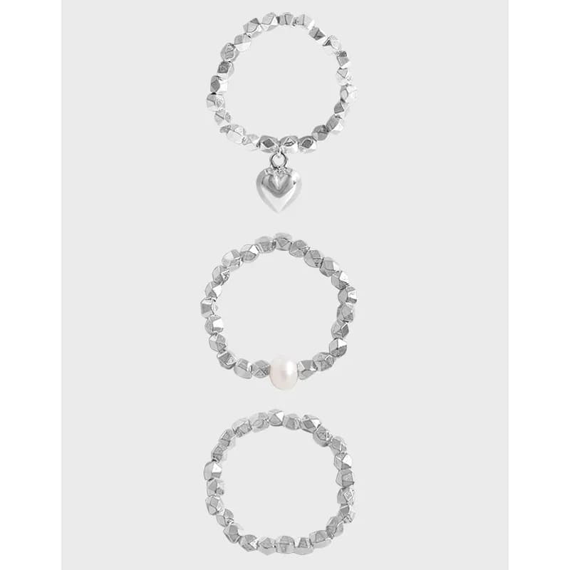 Three sterling silver rings with faceted bead bands, one with a heart charm, one with a pearl, and one plain, displayed vertically.