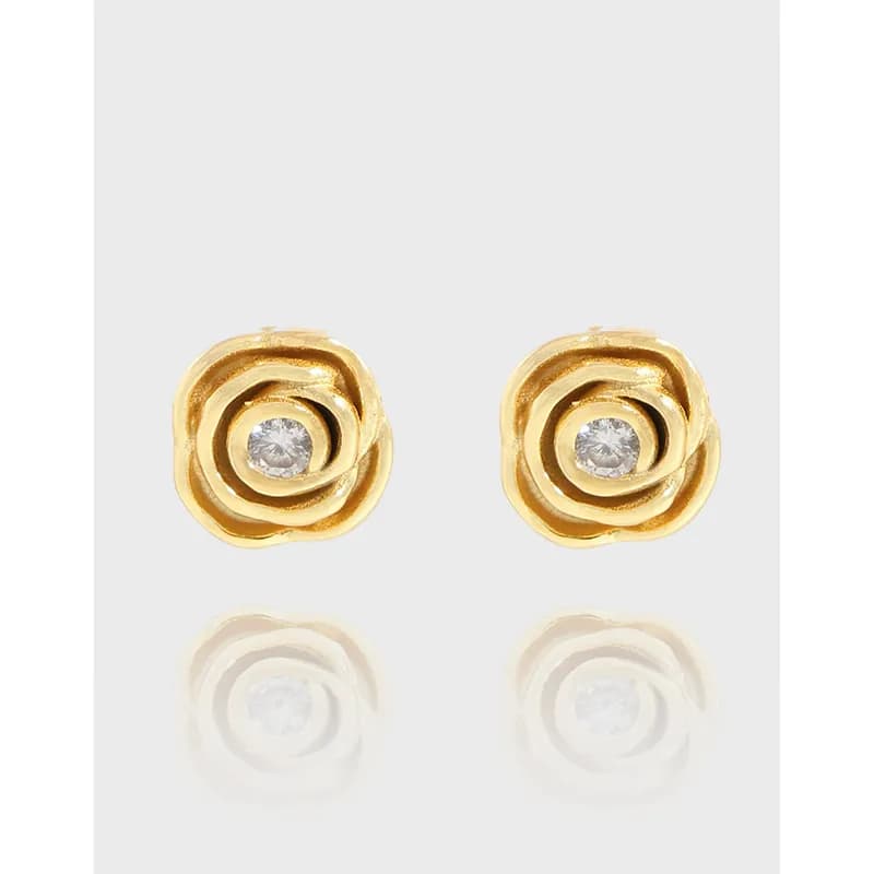 Pair of gold-tone rosette stud earrings with a clear central stone against a light backdrop.