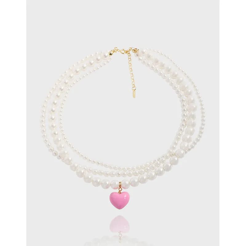 Three-strand pearl necklace with a pink heart pendant and gold-tone extender clasp.
