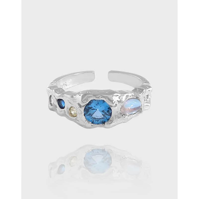 Polished sterling silver ring with a central blue gemstone and smaller stones set along an irregular, textured band.
