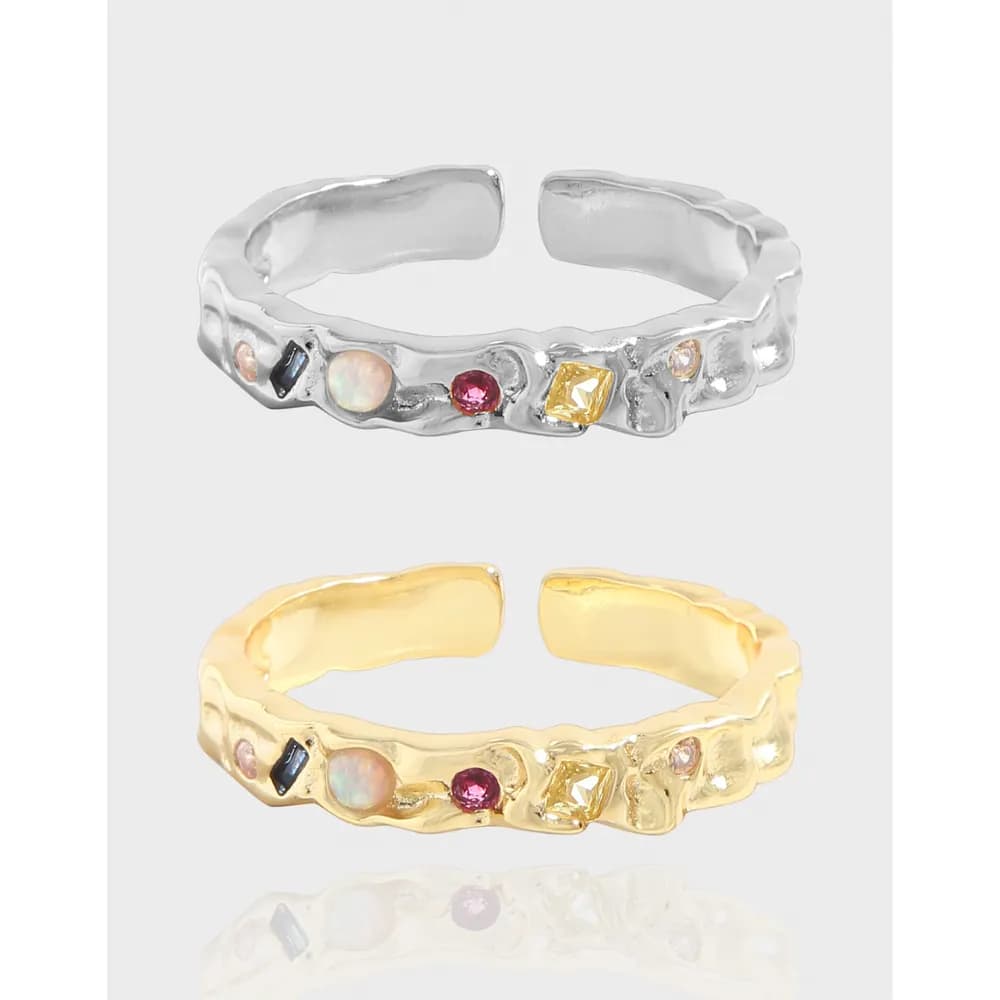 Polished silver and gold-tone rings with an irregular band and assorted small gemstones along the front