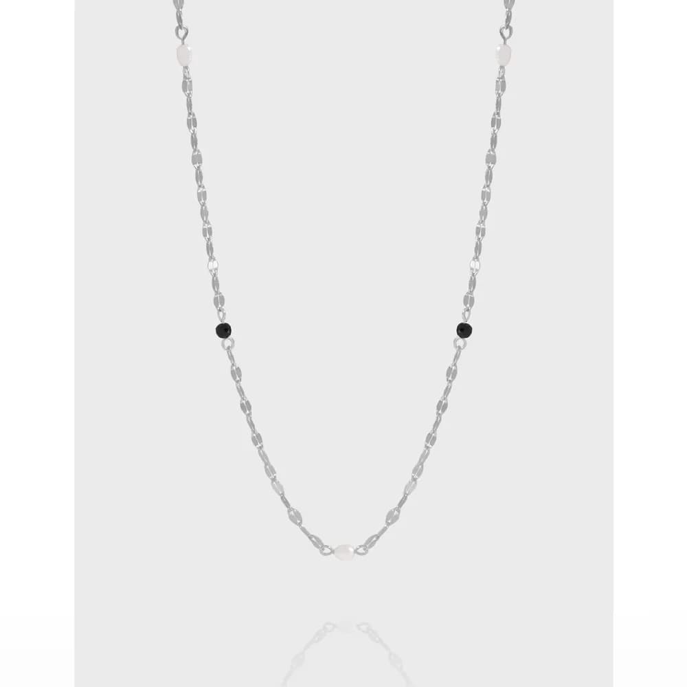 Silver chain necklace with a white pearl bead centered near the bottom and two small black beads along the chain.