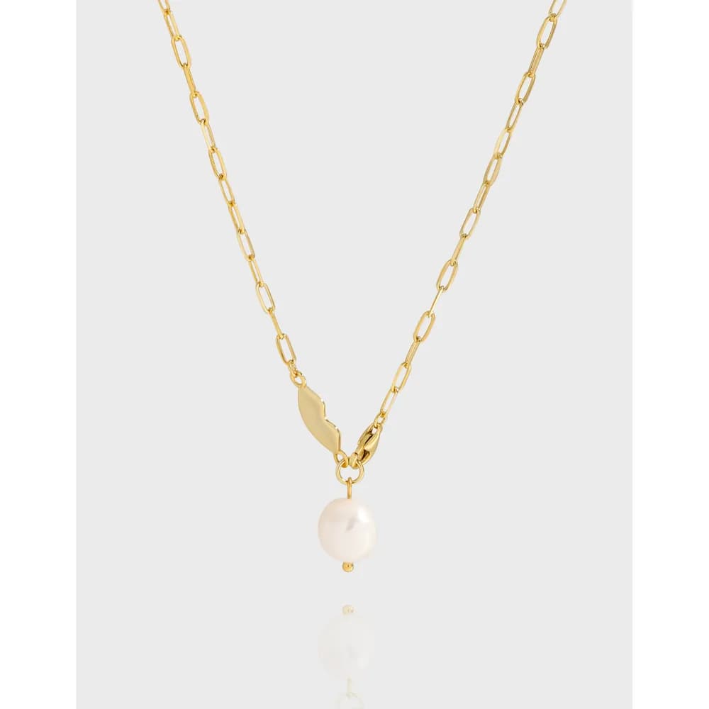 Gold-tone chain necklace with a single white pearl drop and small leaf accent on a light background.