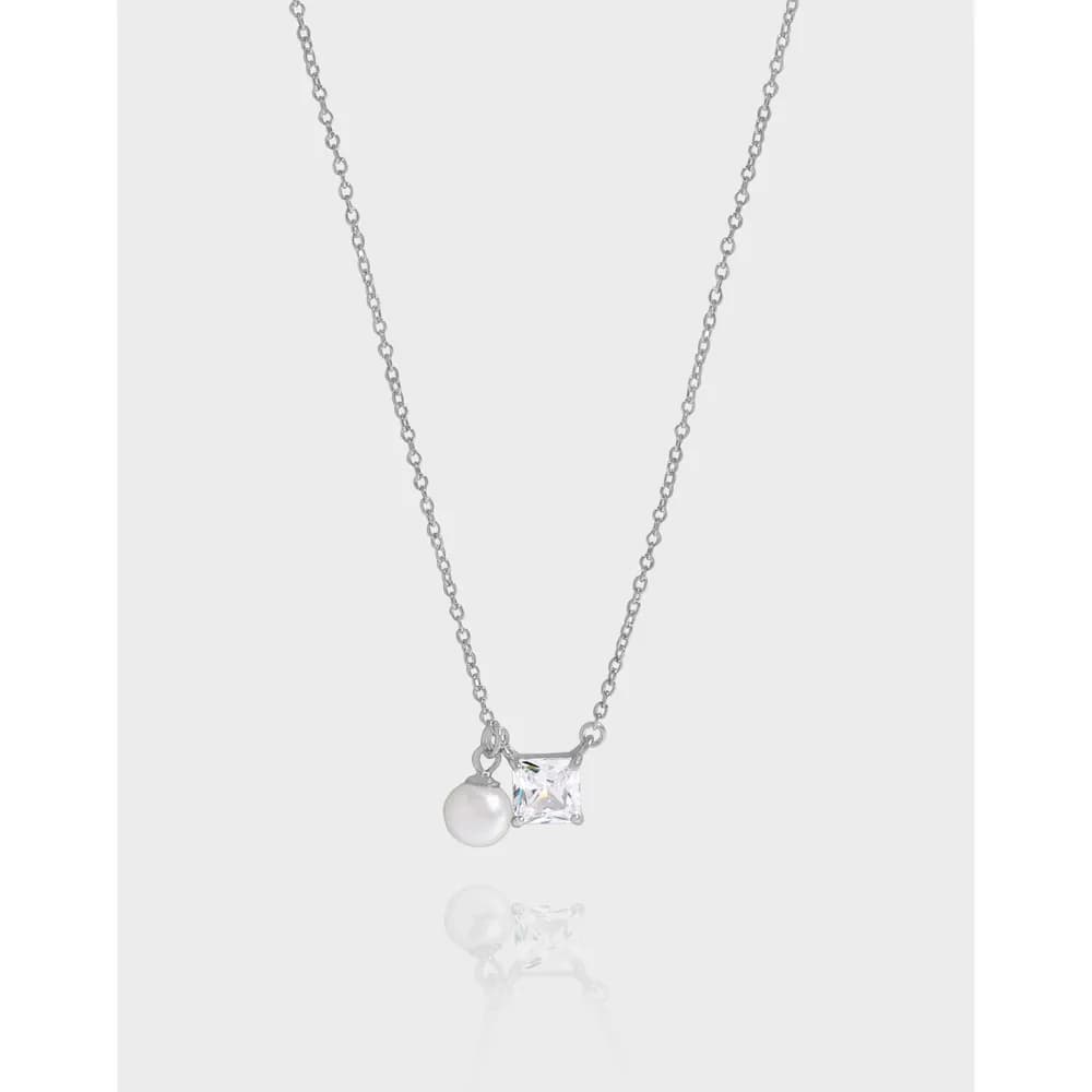 Silver necklace with a pearl and square crystal pendant hanging against a light background.