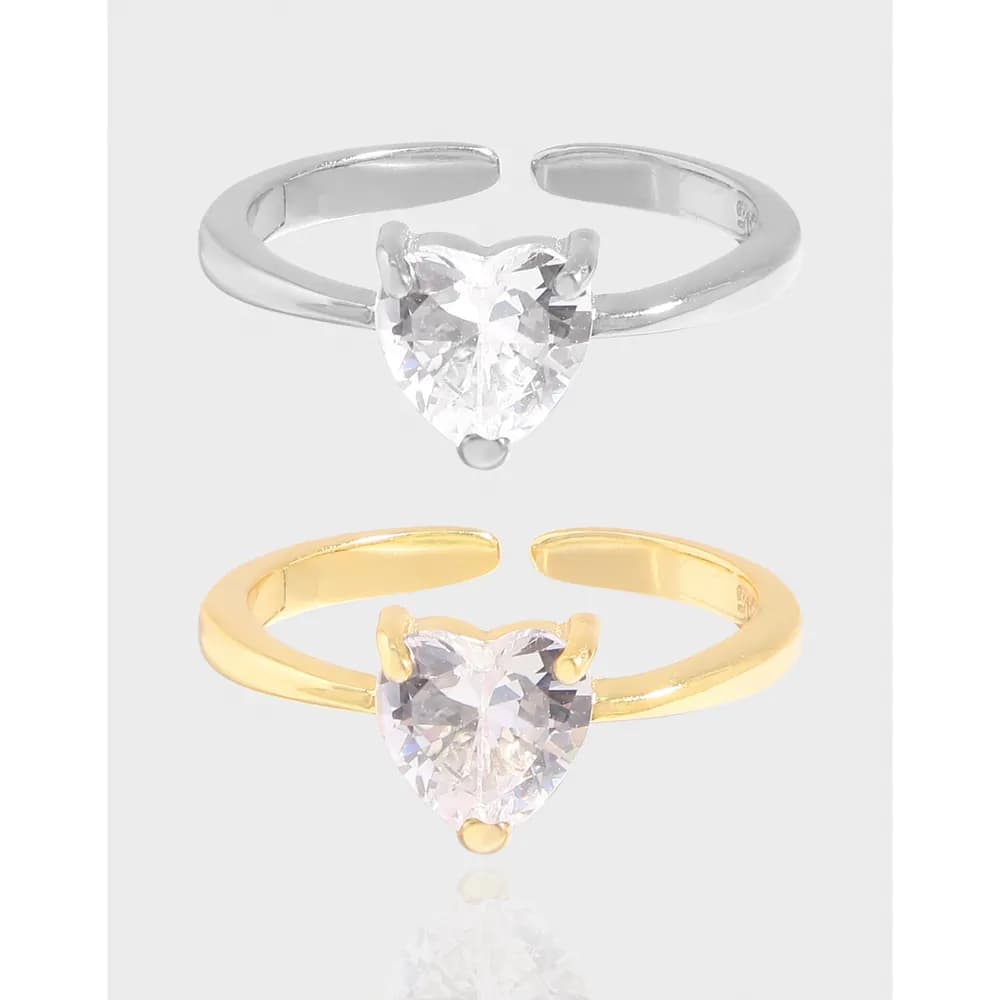 Two rings, silver and gold-tone, with a heart-shaped clear gemstone set in prongs on an open band.