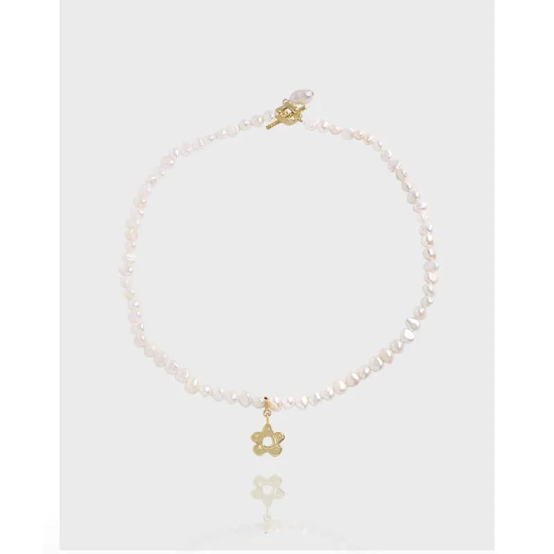Close-up of a pearl bead necklace with a gold-tone flower charm and a small gold clasp.