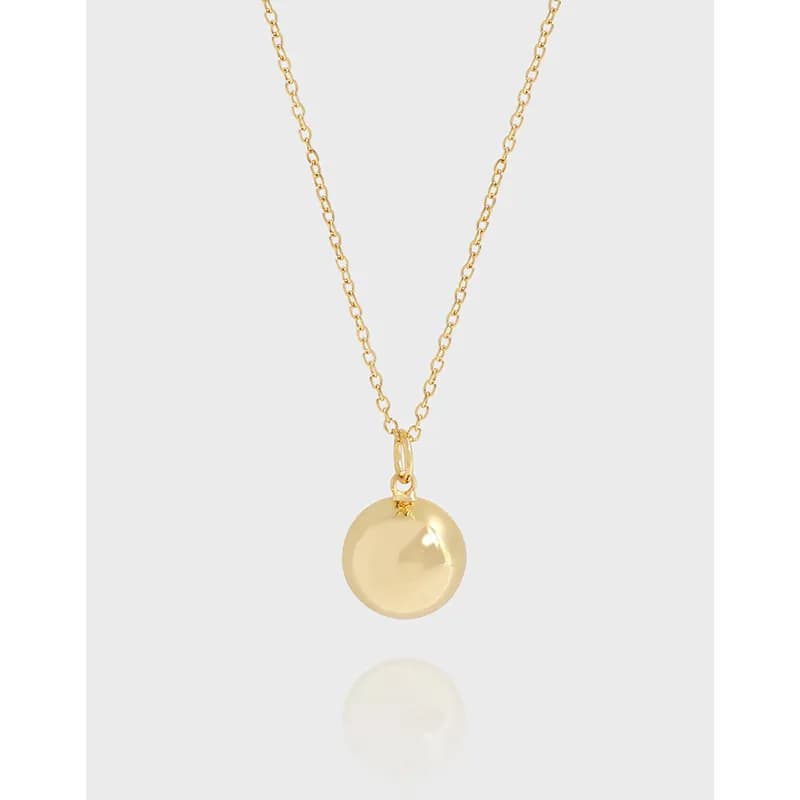 Delicate gold-tone necklace with a round polished pendant on a light background.