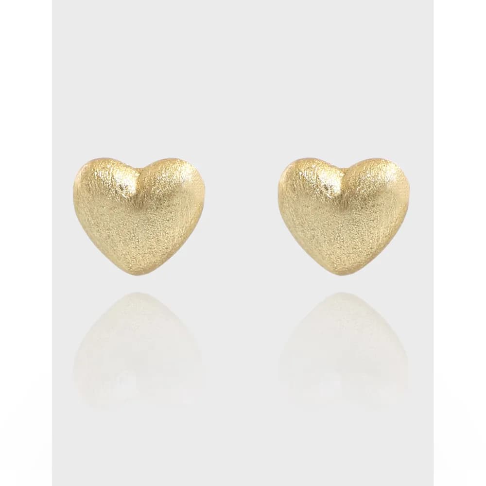 Two gold-toned heart-shaped stud earrings with a textured finish sitting on a light gray background.