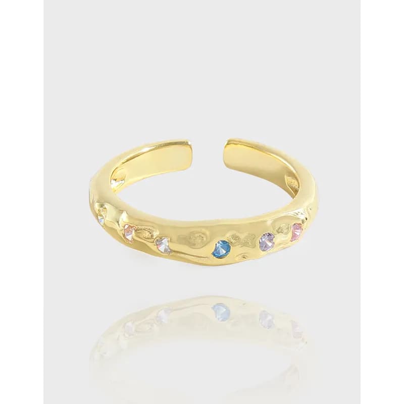 Open cuff ring in polished metal with small multicolor stones along the band on a white background.