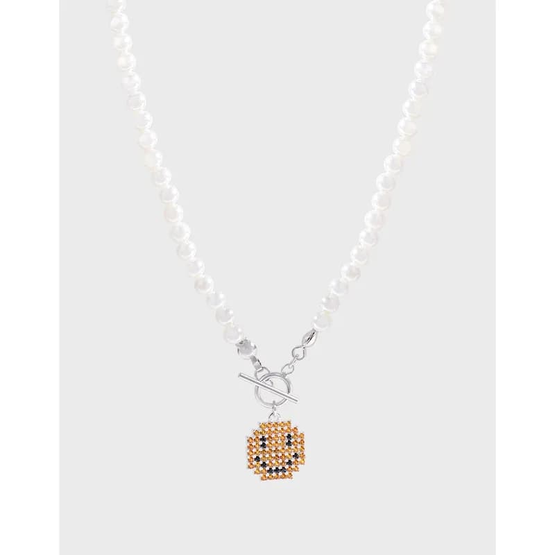 Pearl bead necklace with a small beaded emoji pendant hanging from a toggle clasp.