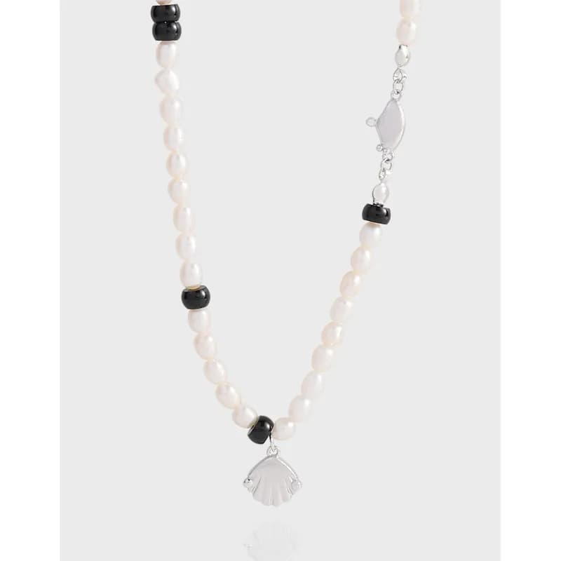 Pearl bead necklace with black spacer beads and a silver scallop shell pendant on a light background.