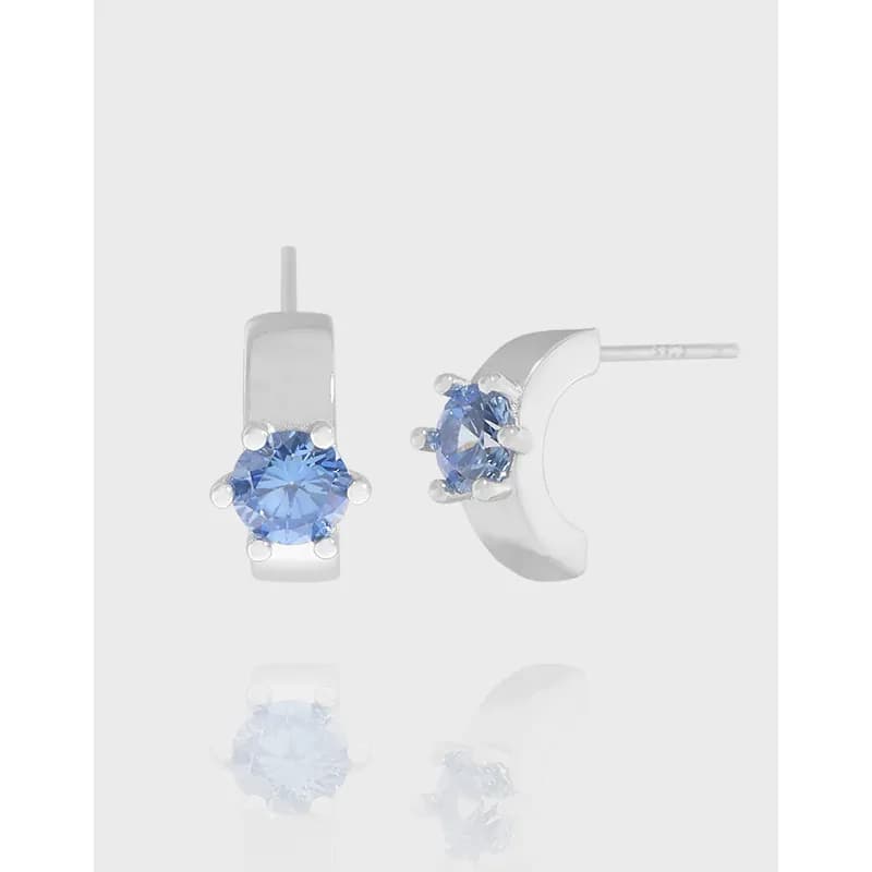 Polished sterling silver drop earrings with a round blue gemstone set in a four-prong setting on a vertical bar.