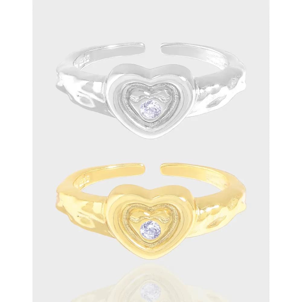 Open-ended heart ring with a double-heart motif and a central clear gemstone in polished metal.