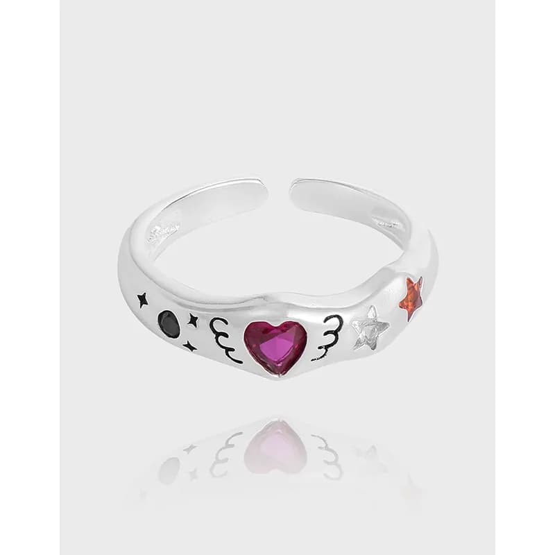 Open silver ring with a pink heart gemstone and star and moon charms along the band.