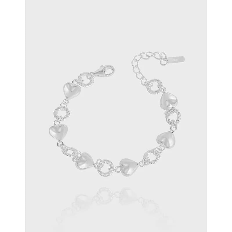 Polished sterling silver bracelet with heart charms and linked chain against a light background.