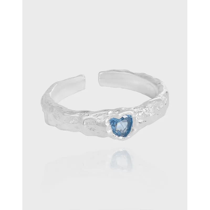 Textured sterling silver ring with a blue heart-shaped gemstone on a light background.