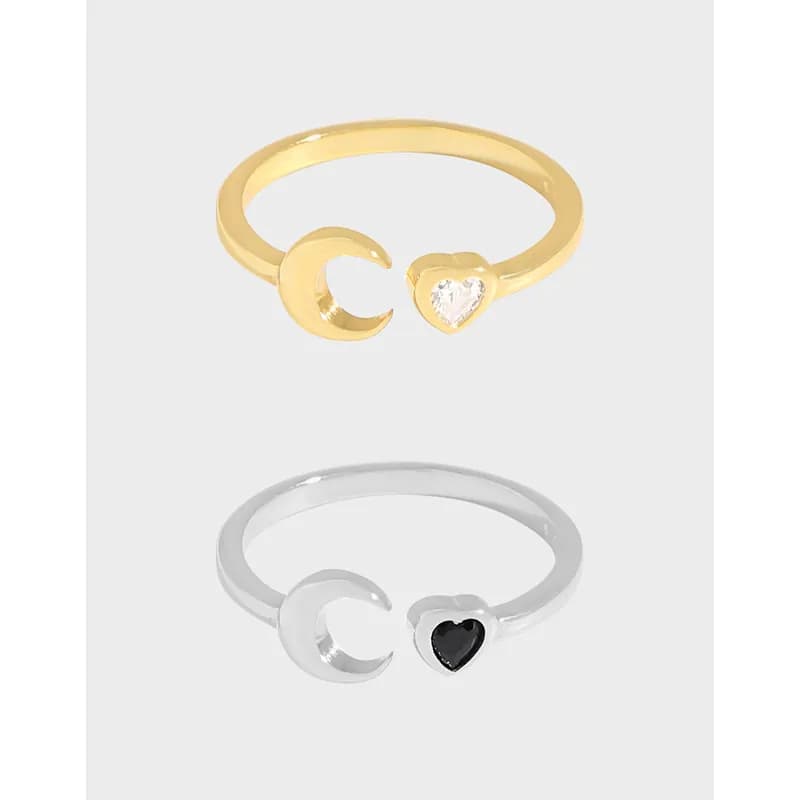 Open crescent moon and heart ring with contrasting ends, one featuring a clear stone on a gold-tone finish and the other a dark stone on silver.