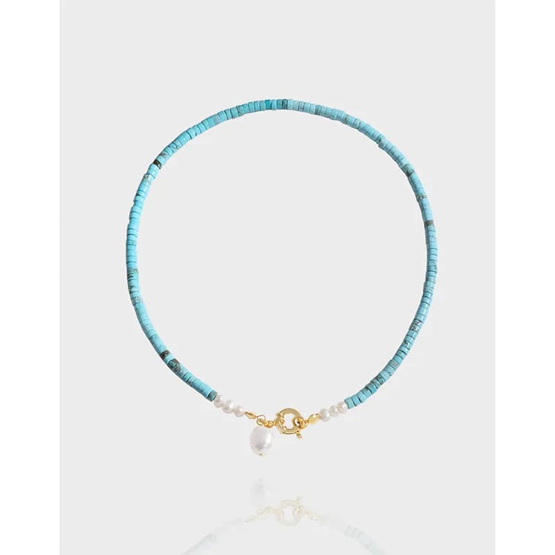 Turquoise beaded necklace with a small pearl charm and gold clasp photographed on a light background.