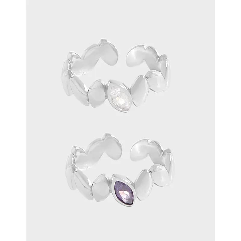 Open petal-link sterling silver ring with teardrop stones, one clear and one purple, shown on a pale background.