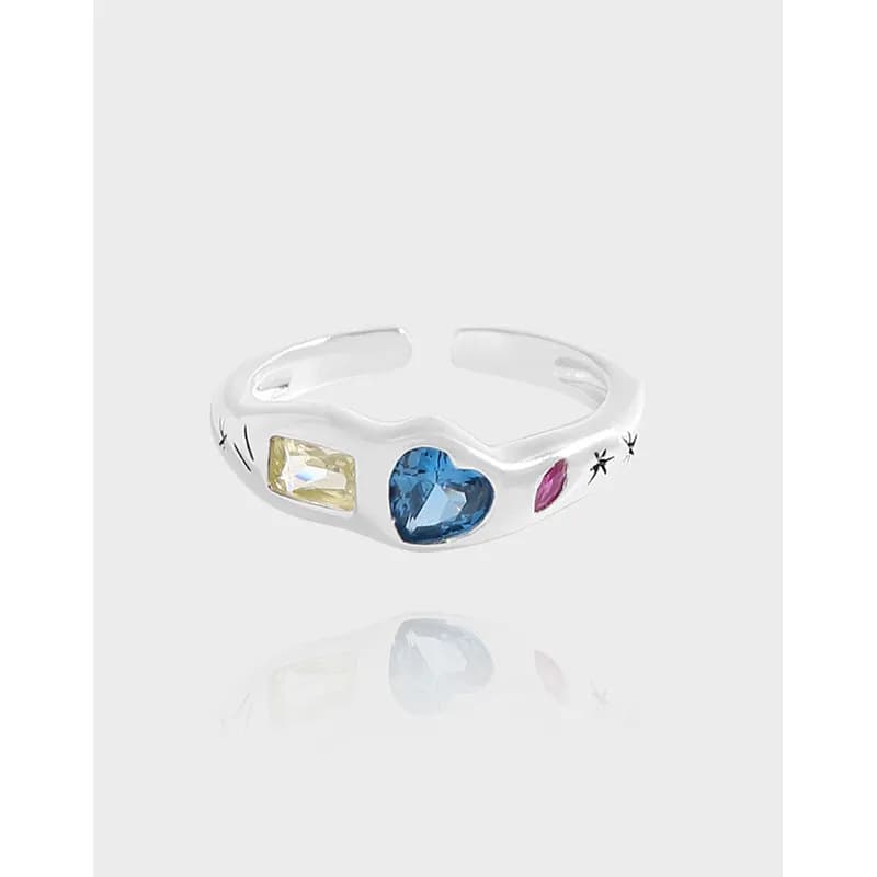 Polished silver ring featuring a blue heart gemstone with yellow and pink side stones on a curved band.