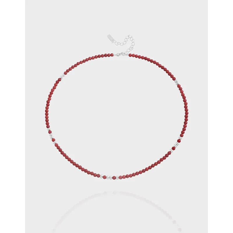 Red beaded necklace with silver spacer beads and an adjustable extender chain laid flat.