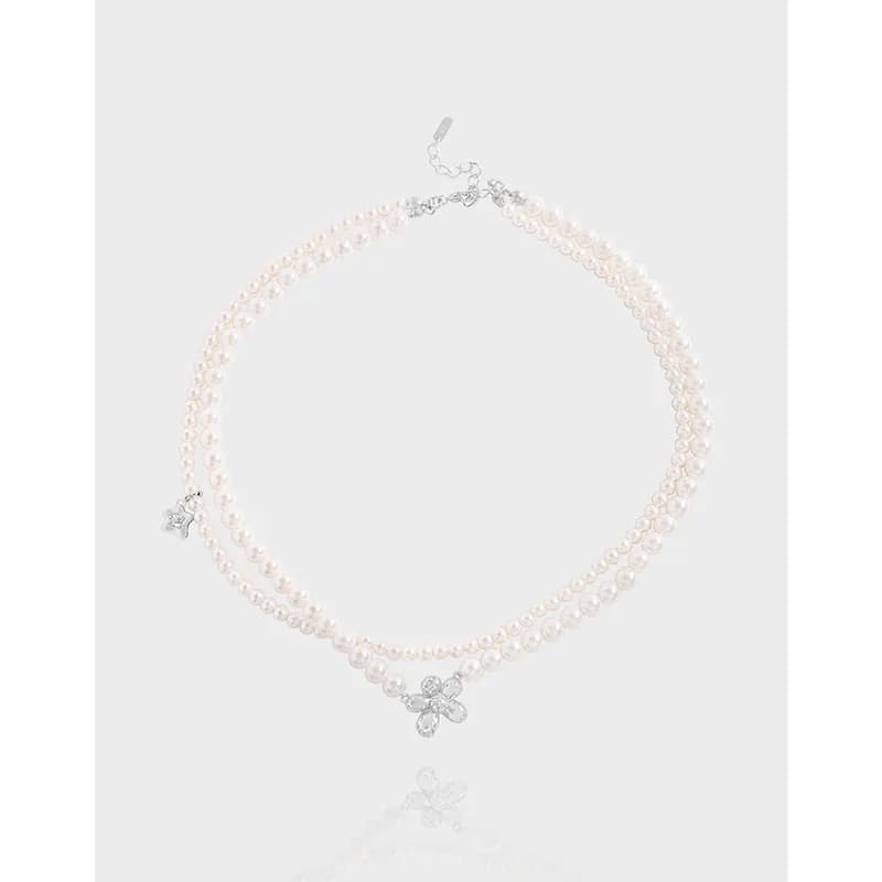 Two-strand pearl necklace with a silver crystal flower pendant against a light background.
