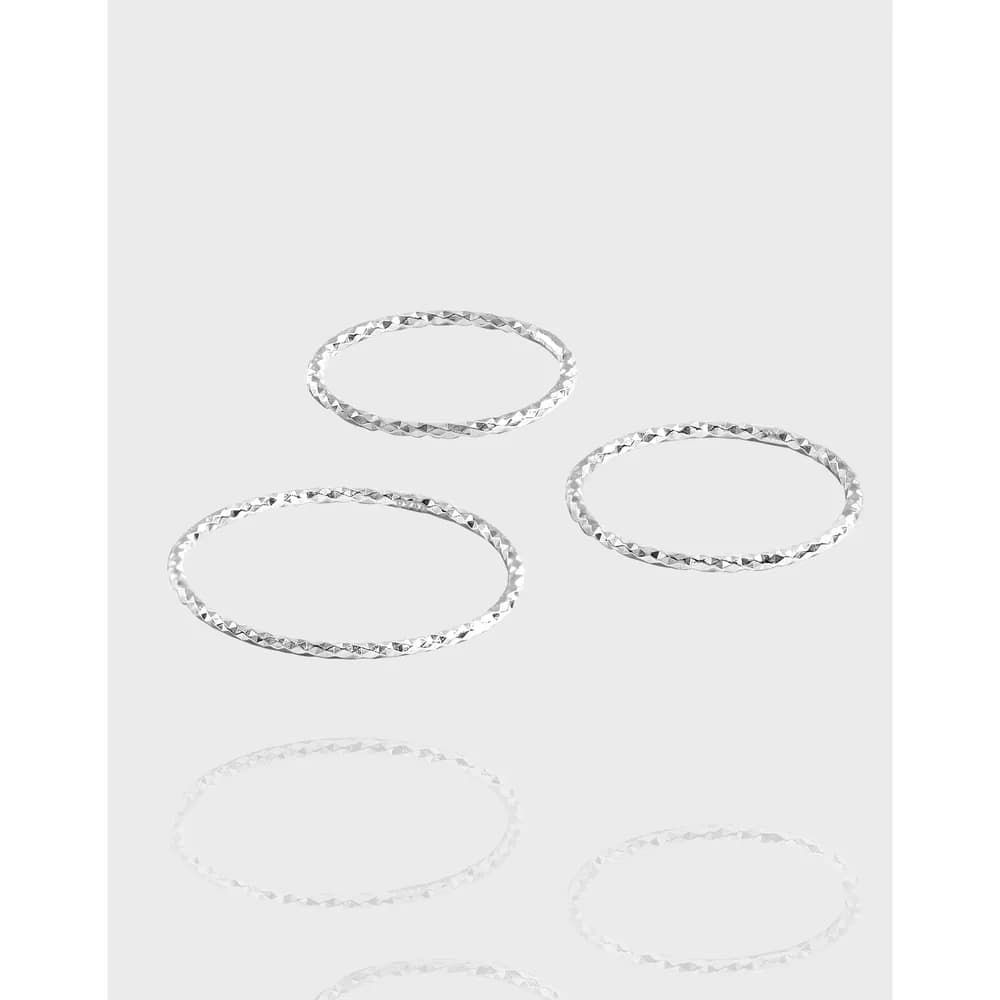 Four slender hammered sterling silver rings arranged on a pale background.