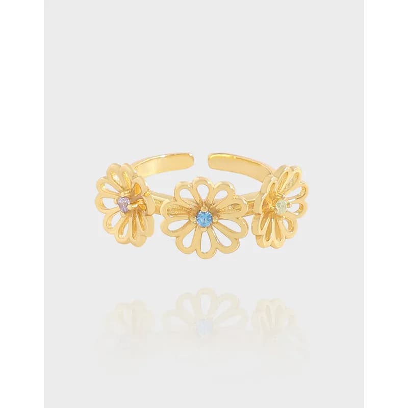 Three daisy-shaped flowers linked along a slim ring band with pastel stone centers, shown in polished metal.