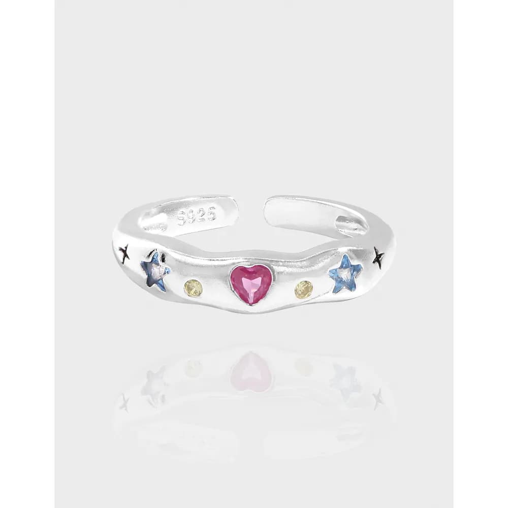 Open sterling silver ring featuring a pink heart center with blue stars and small yellow stones along the band.