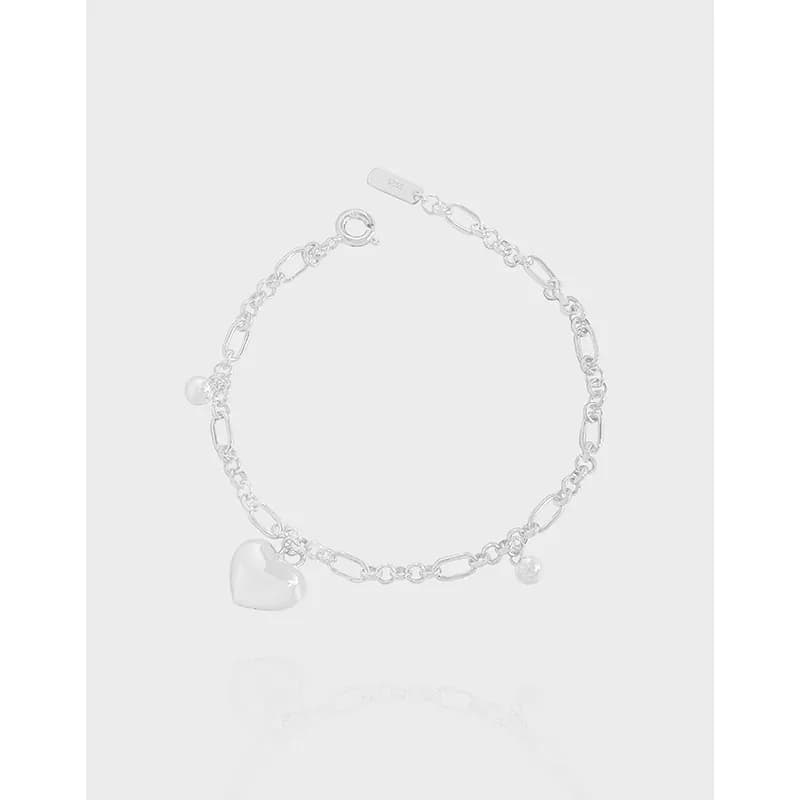 Polished sterling silver chain bracelet with a heart charm and small bead charm on a plain background.