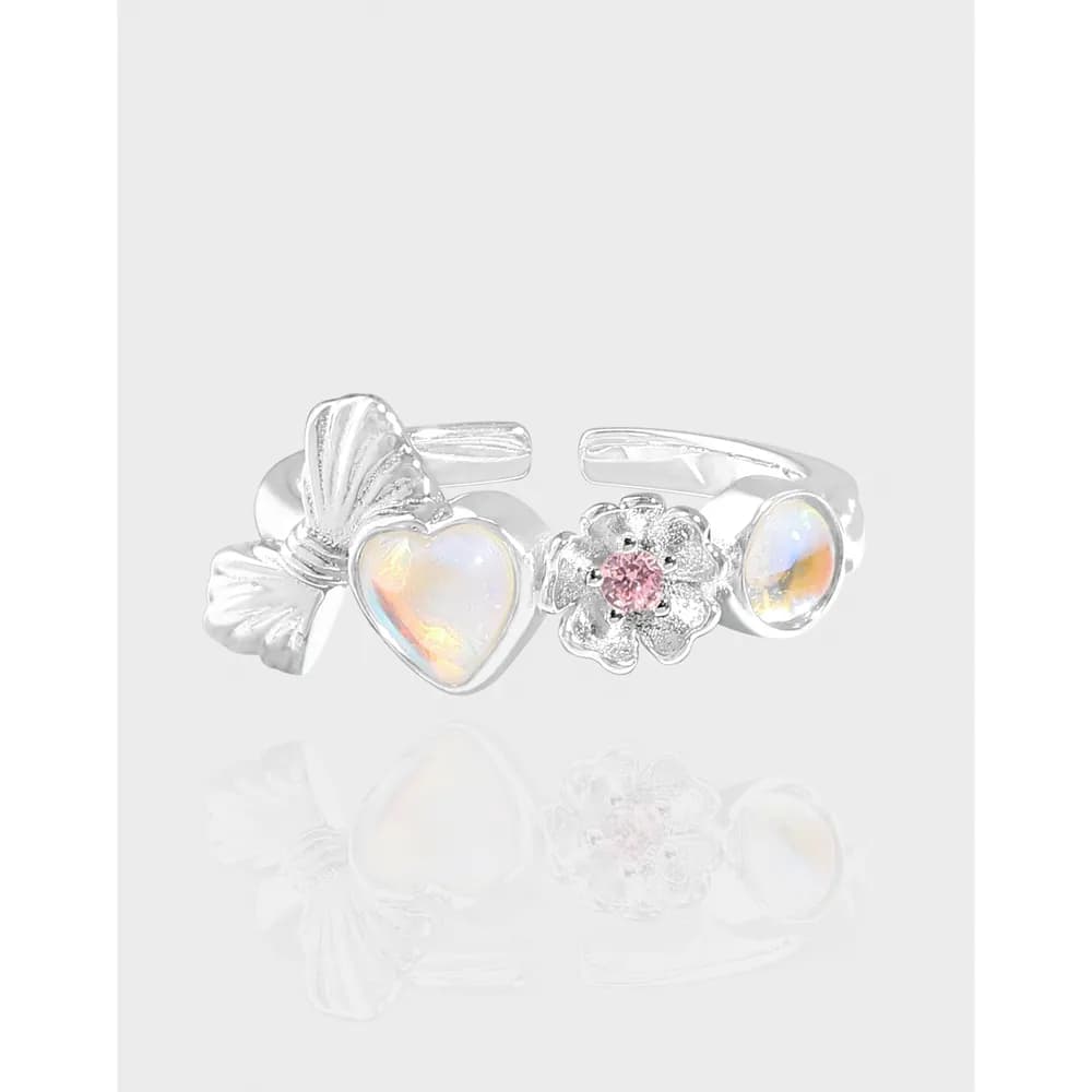 Open sterling silver ring with three charms including a heart opal, a pink-centered flower, and an oval opalescent accent