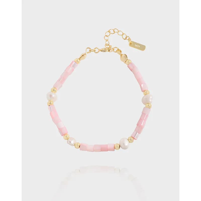 Close-up of a pink enamel and pearl bracelet with gold-tone spacers and an adjustable chain