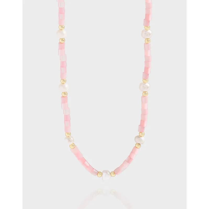 Delicate pink enamel bead necklace with pearls and gold spacers on a light background.