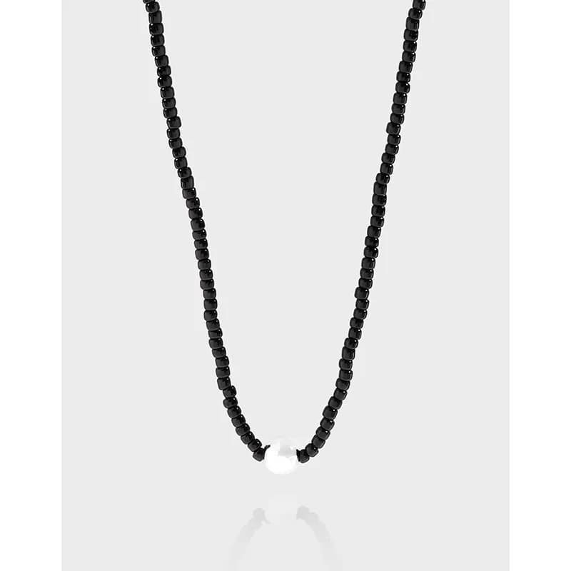 Close-up of a polished black bead necklace with a single white pearl centerpiece against a light gray background.