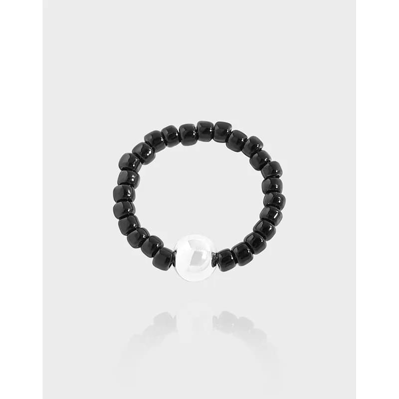 Polished beaded ring with black beads and a clear central accent bead on a light background.