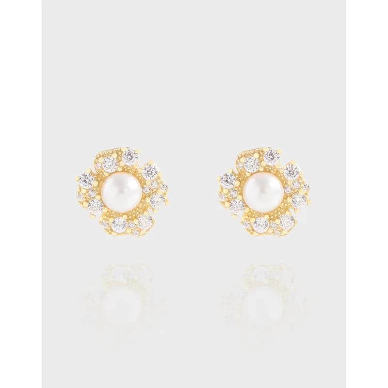 A pair of pearl-centered stud earrings with a circular halo of small crystals on a polished metal setting.
