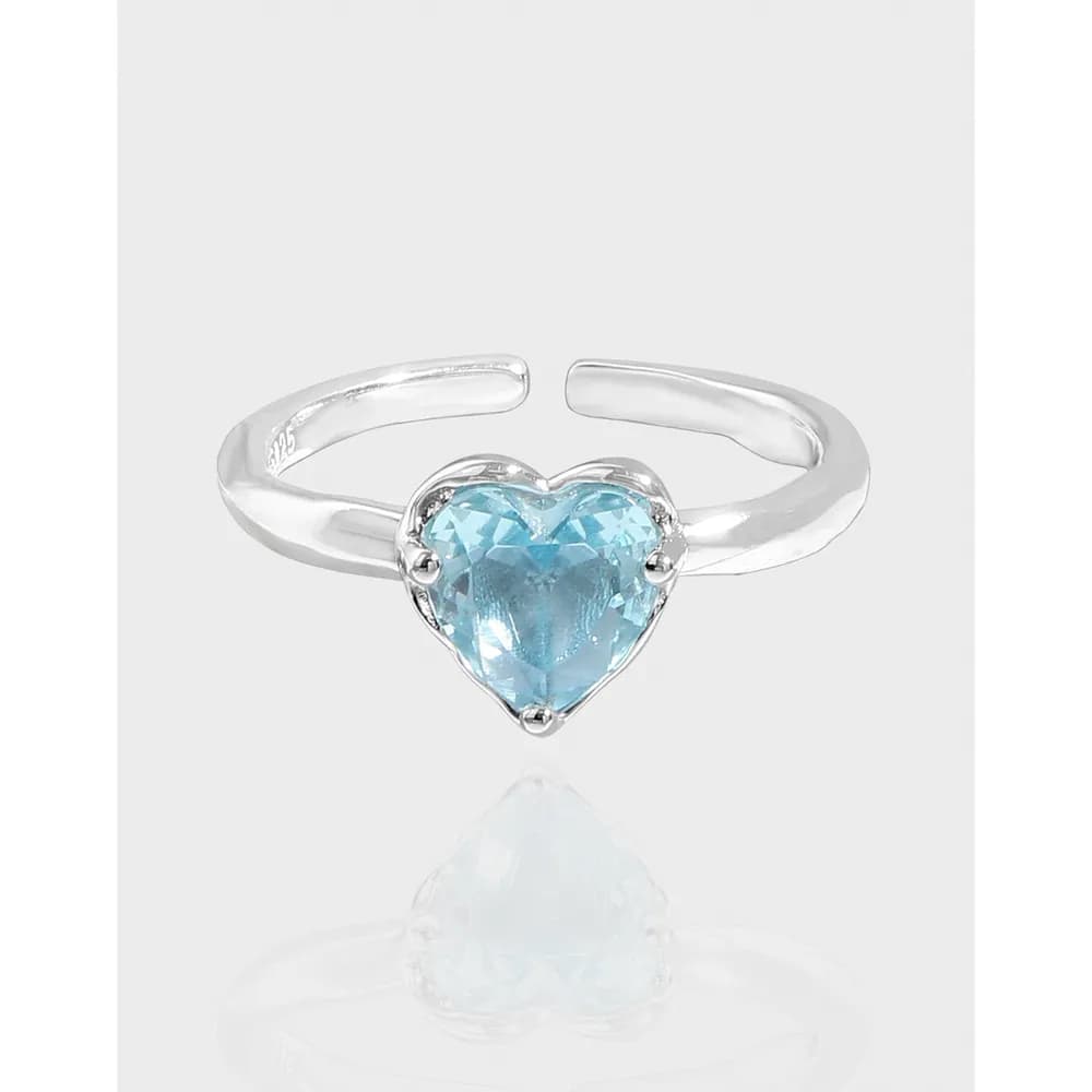 Open, adjustable silver ring with a heart-shaped blue faceted gemstone at the center.