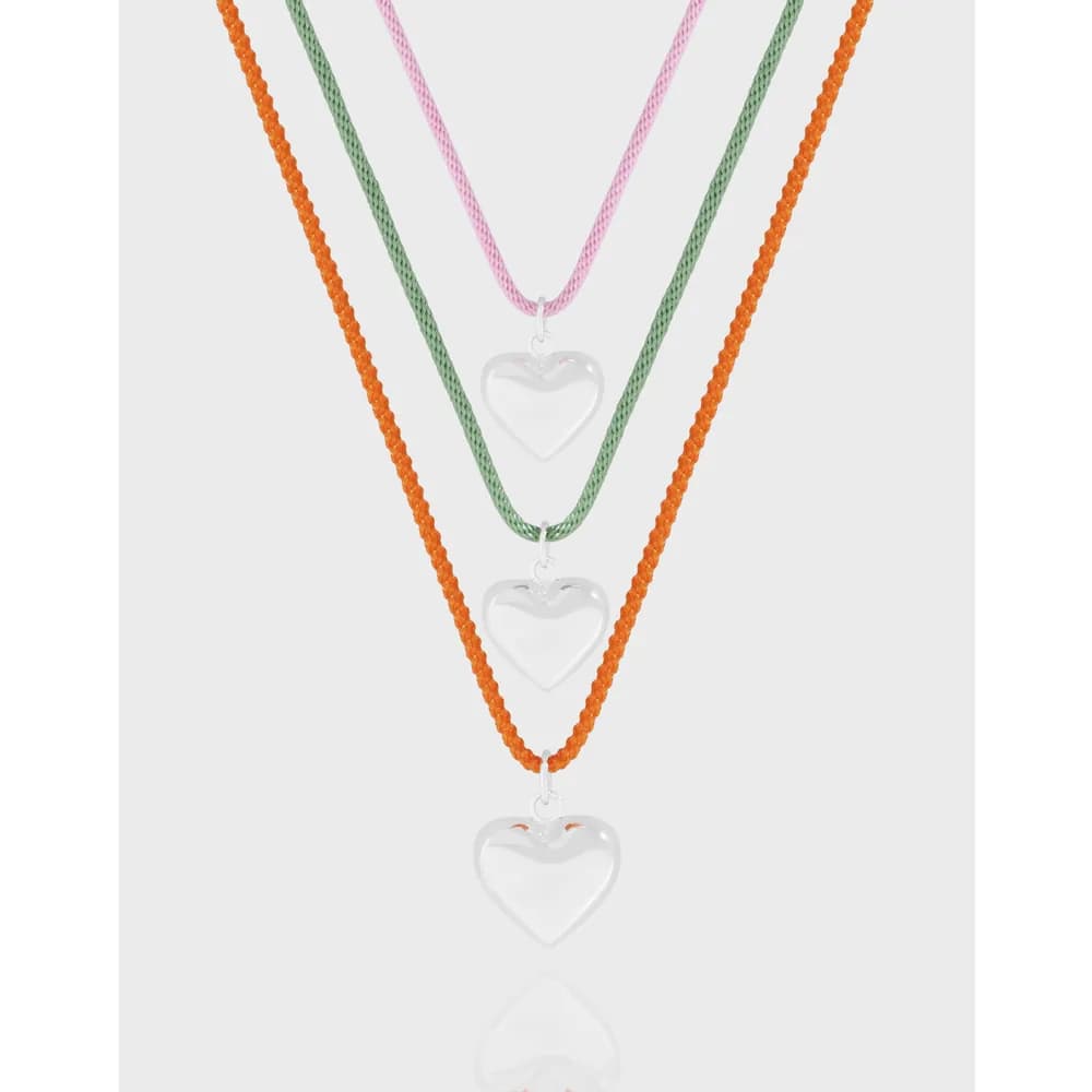 Three layered necklaces with hollow silver heart pendants on orange beaded, green, and pink cords.