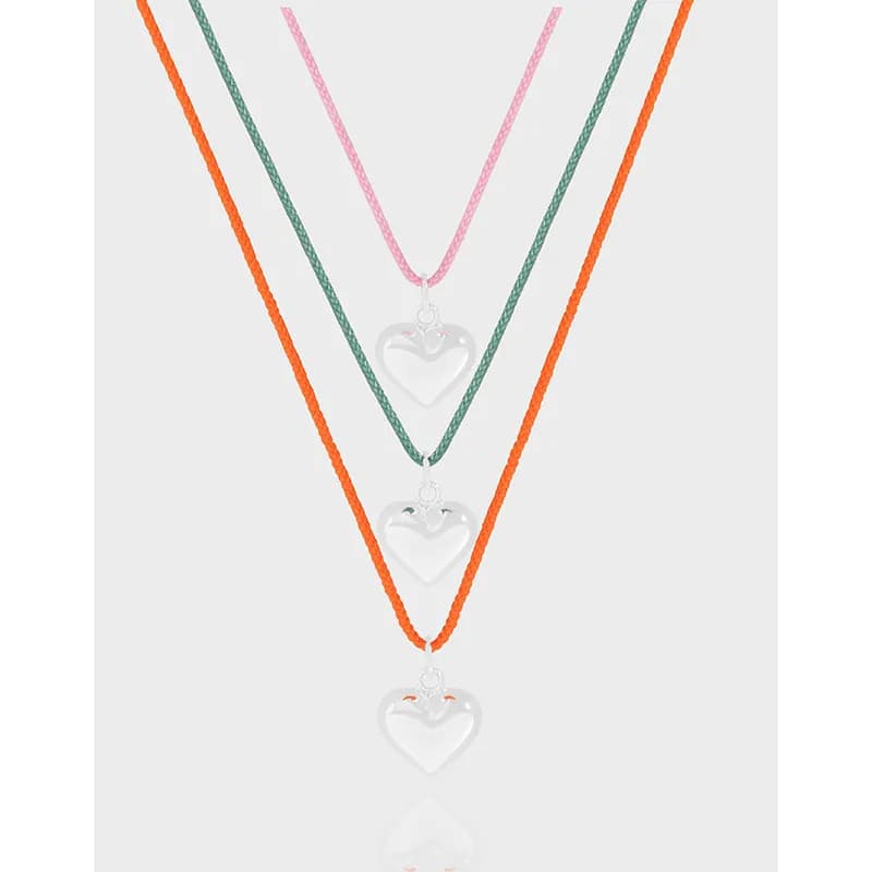 Layered necklace with three silver heart pendants on pink, green, and orange enameled cords