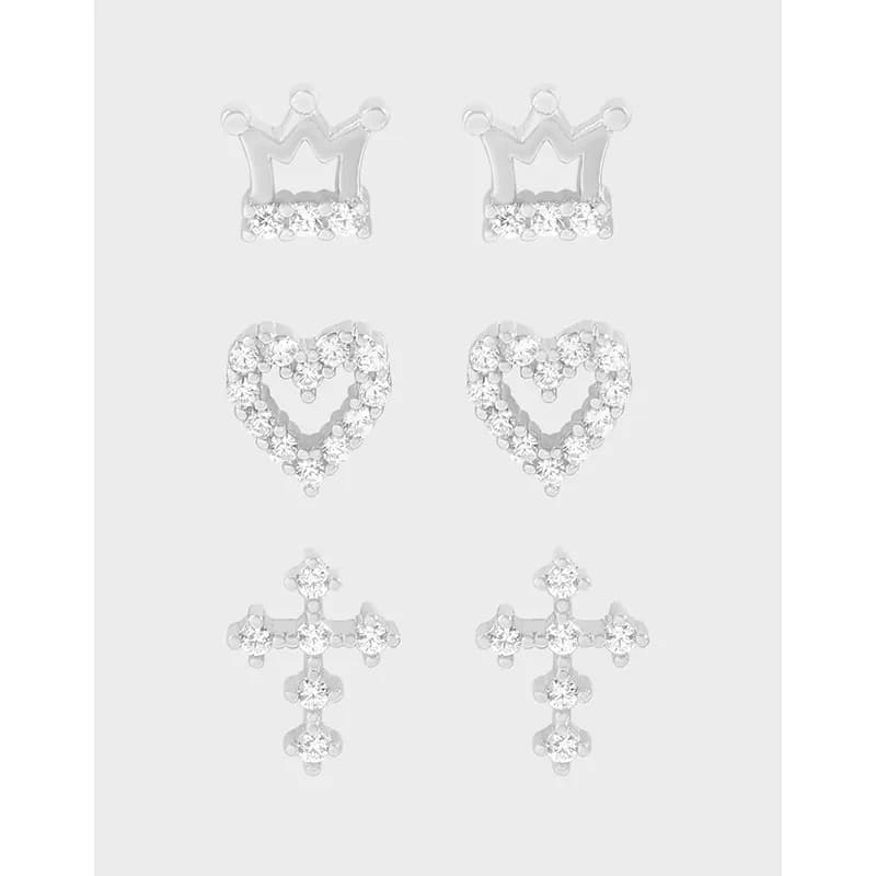 Close-up of three sterling silver stud earrings in crown, heart, and cross shapes with crystals.
