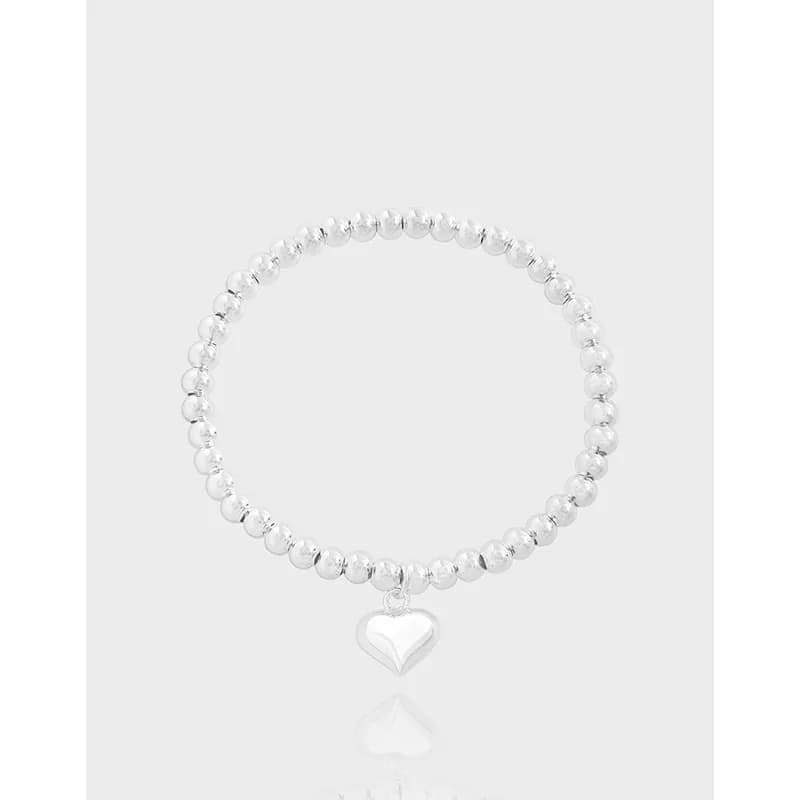 Sterling silver beaded bracelet with a small heart charm on a pale background.