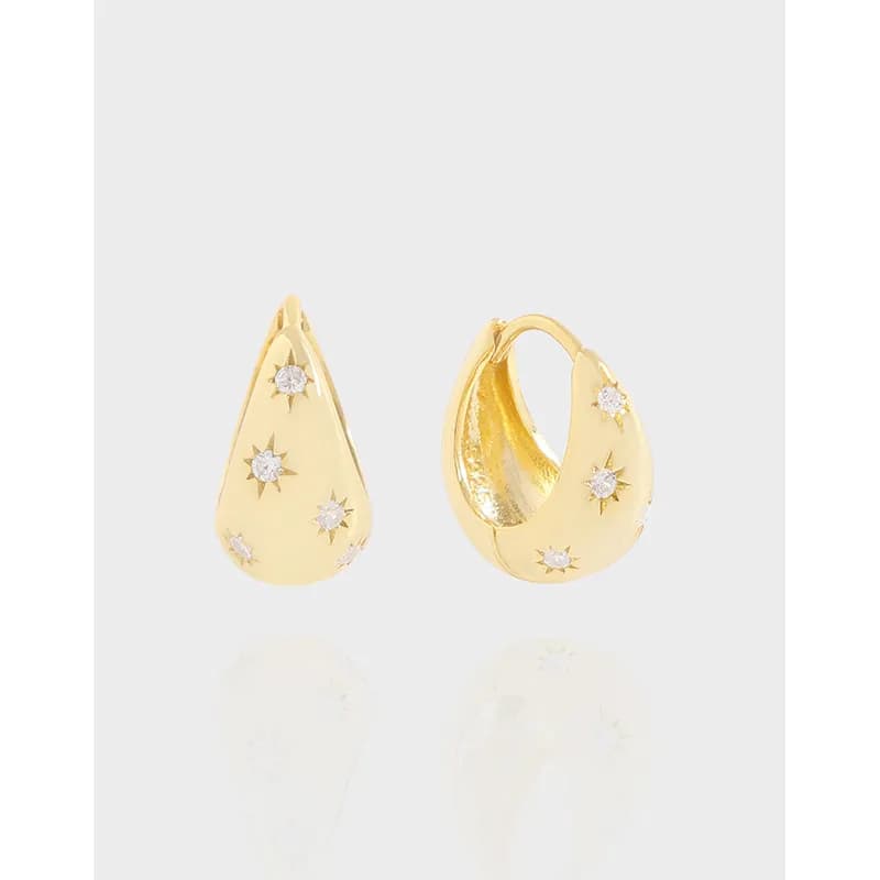 Polished gold-tone teardrop earrings adorned with crystal starbursts on a smooth surface.