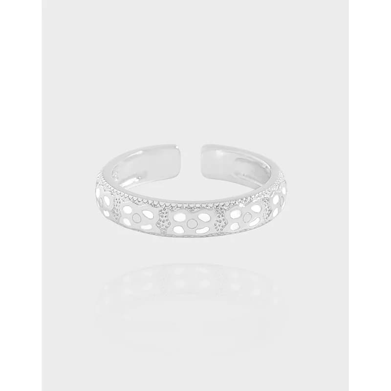 Polished sterling silver openwork ring with circular cutouts and crystal accents on a light background.