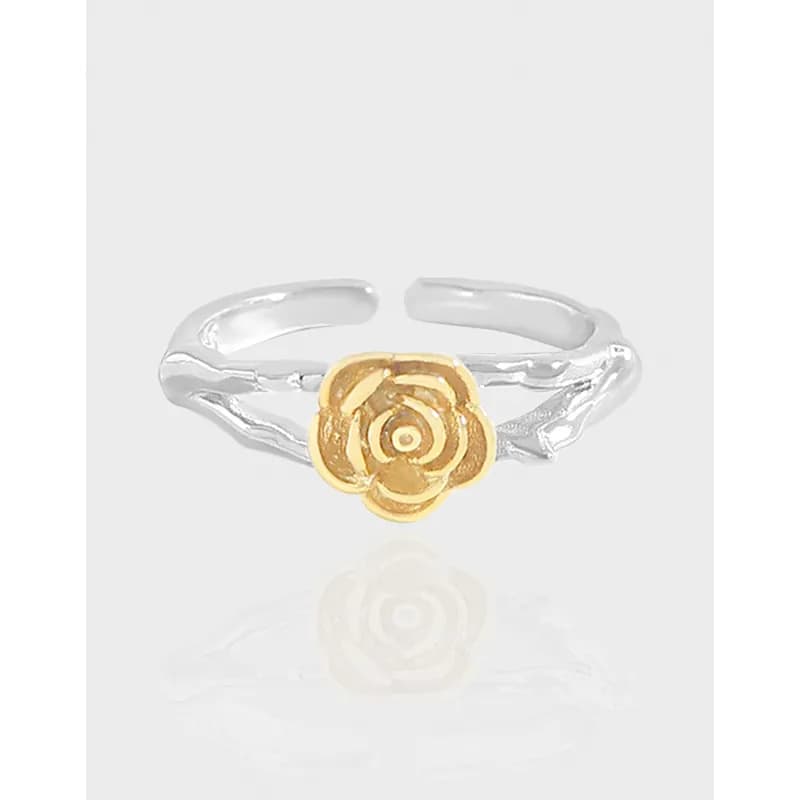 Open silver ring with a gold rose centerpiece on a light background.