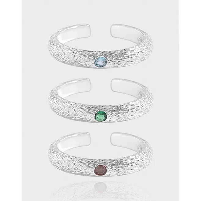 Three textured sterling silver band rings with small bezel-set gemstones in blue, green, and brown displayed in a vertical stack.