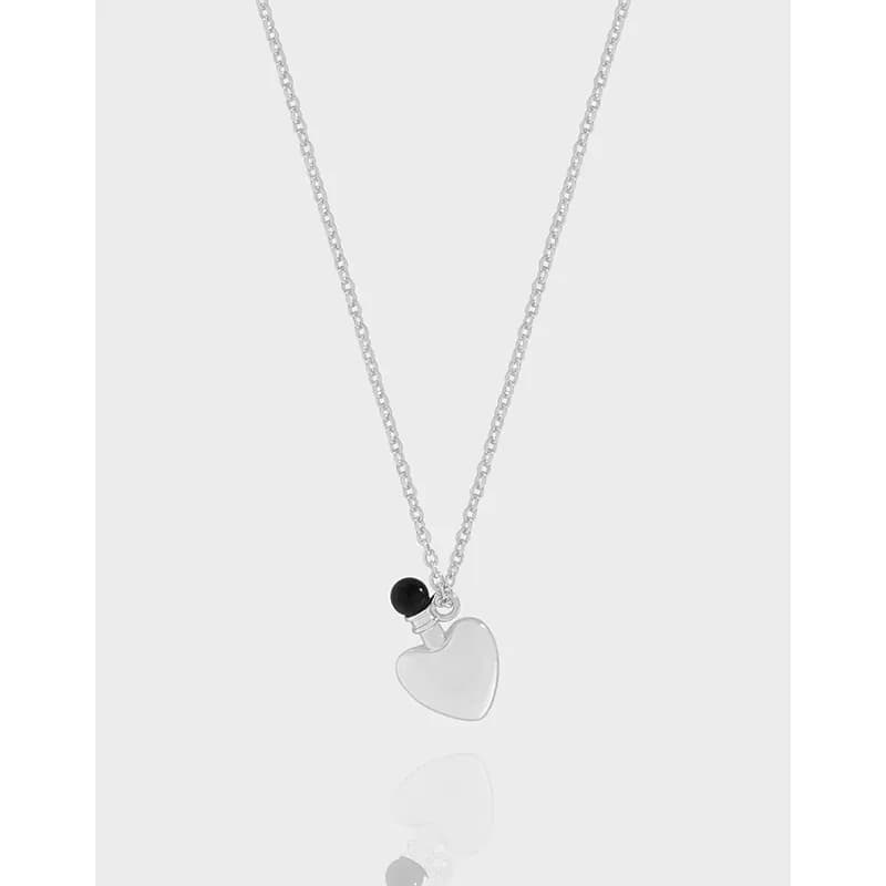 Polished sterling silver necklace with a heart pendant and small black bead against a light background.
