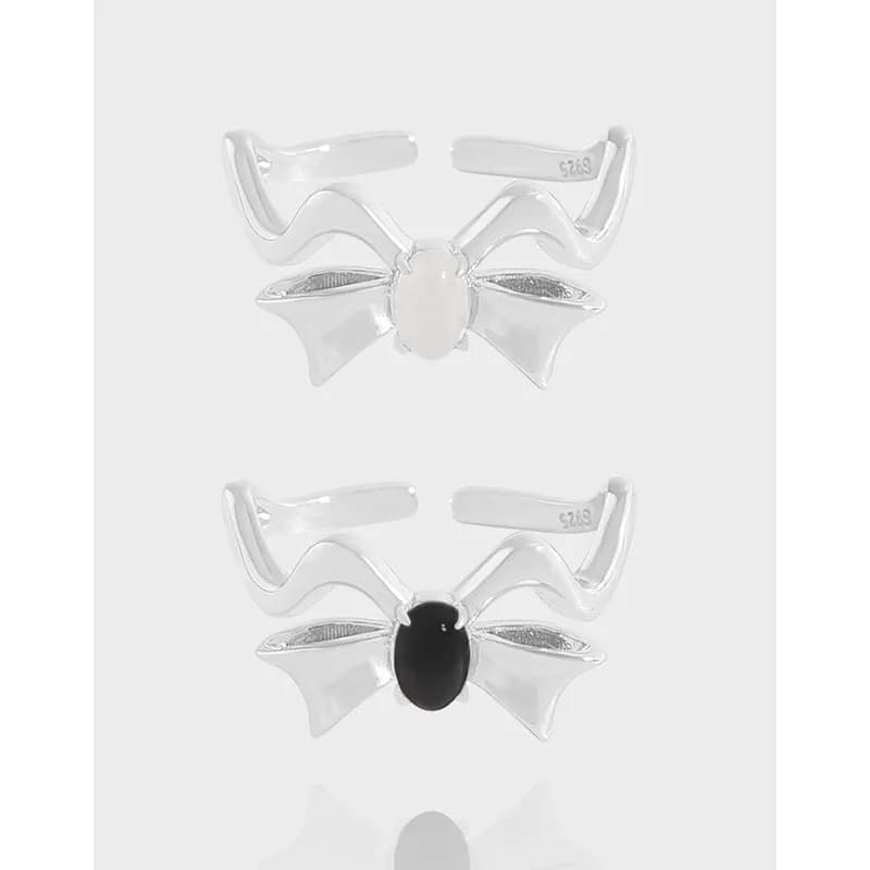 Two Winged Bow Rings in polished sterling silver, one with a white central stone and one with a black central stone.