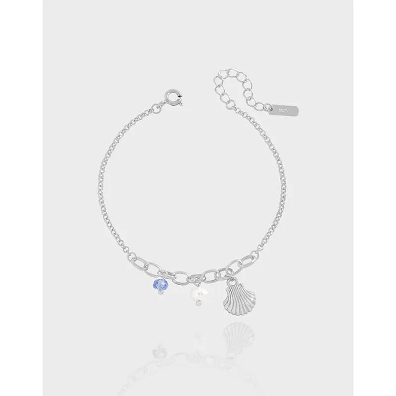 Polished sterling silver bracelet with shell charm, blue bead, and pearl resting on a light background.